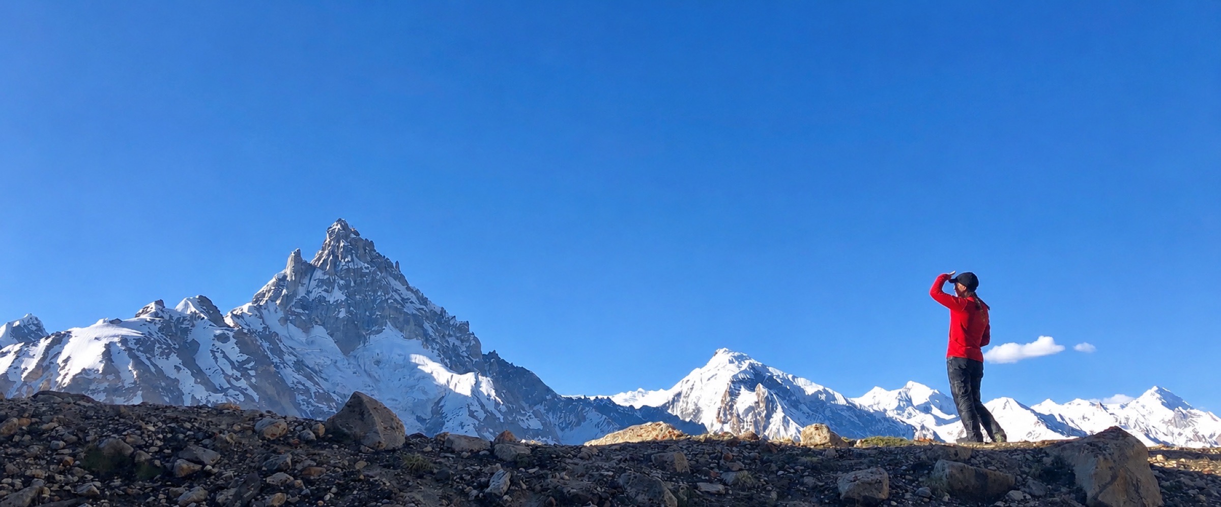 A climber on a rocky ridge looking toward a high snow peak
